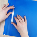 Person using a hole punch on a blue sheet of paper.