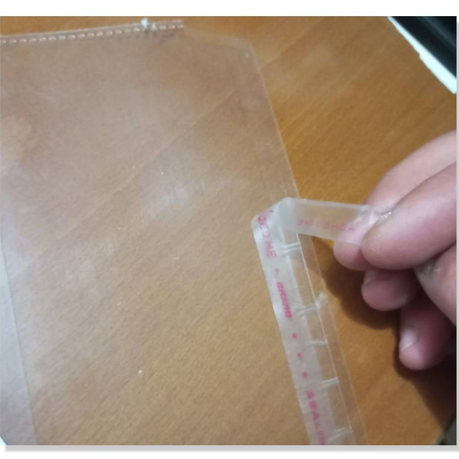 Hand holding a transparent measuring tool with red markings on a wooden surface